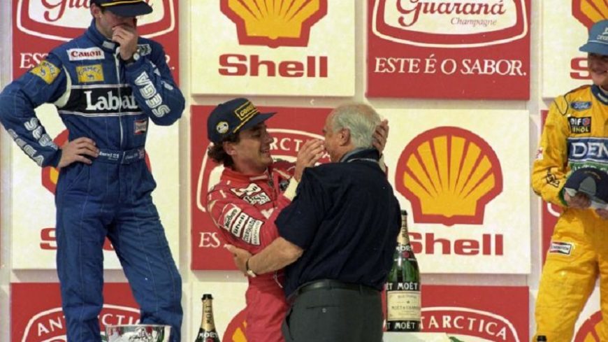 Senna y Fangio se abrazan ante la atenta mirada y admiración de Michael Schumacher